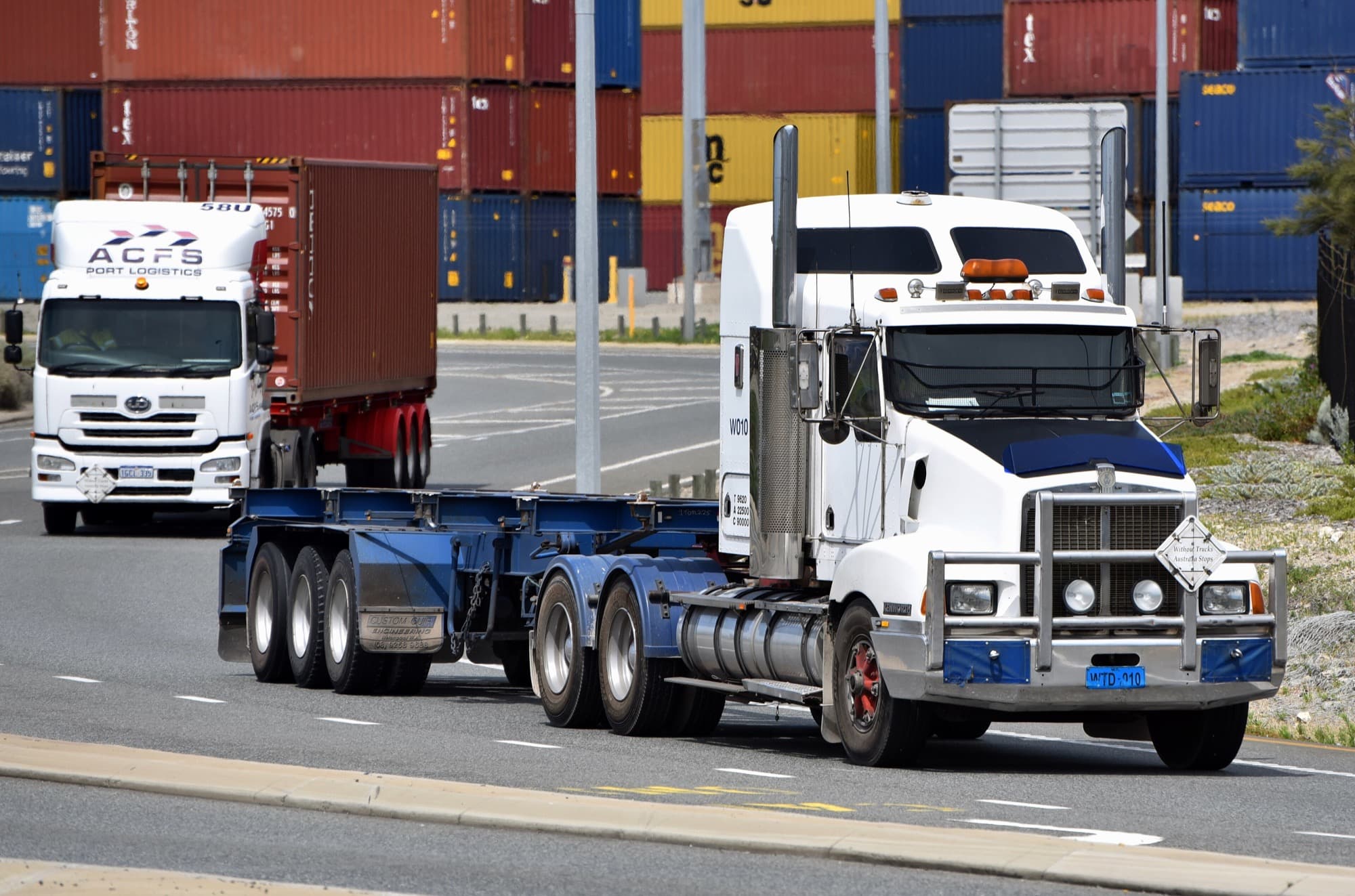 A Kenworth T300 tractor unit, with an unloaded shipping container semi-trailer attached, driving along Port Beach Road, Rous Head, in North Fremantle, Western Australia